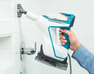 Using handheld steamer with tool to steam shower tile in bathroom.