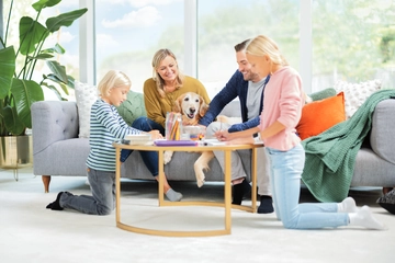 Family and dog around table on carpet in living area.