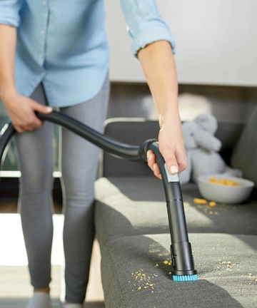 Using dusting brush on hose to vacuum crumbs off couch cushion